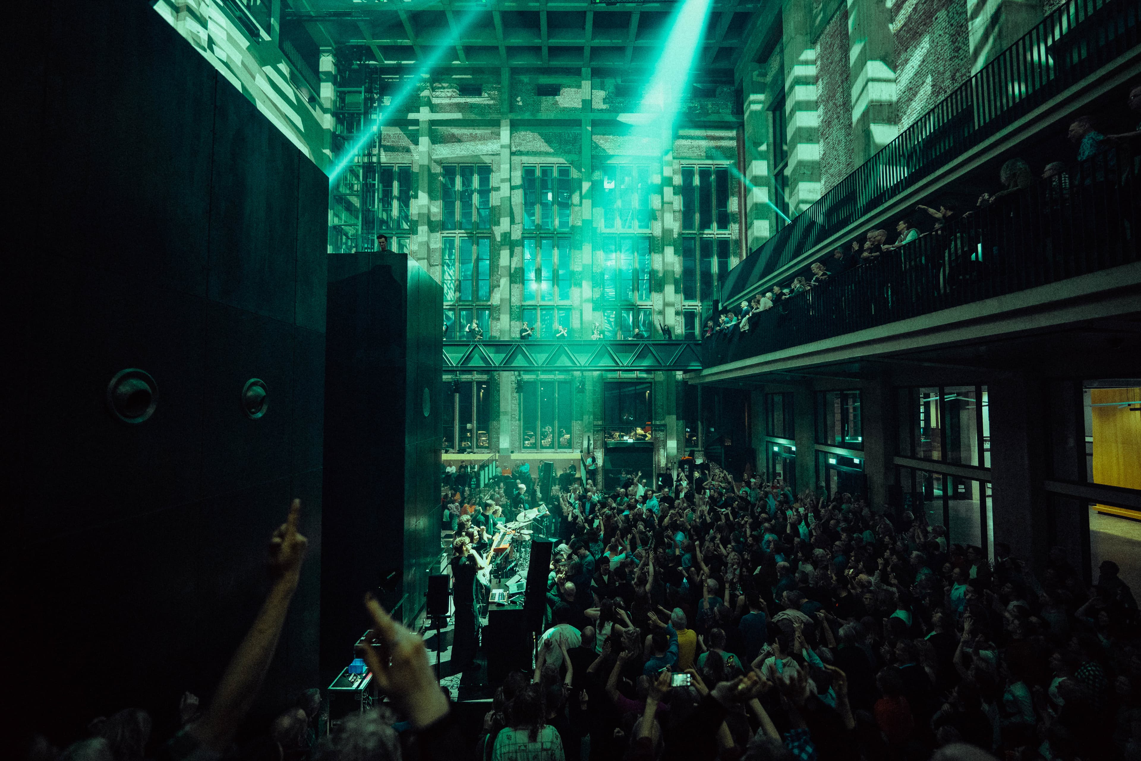 The Jazzrausch Bigband performing amid a standing crowd in the vast industrial Atrium hall at Bergson, lit in coloured stage lighting.