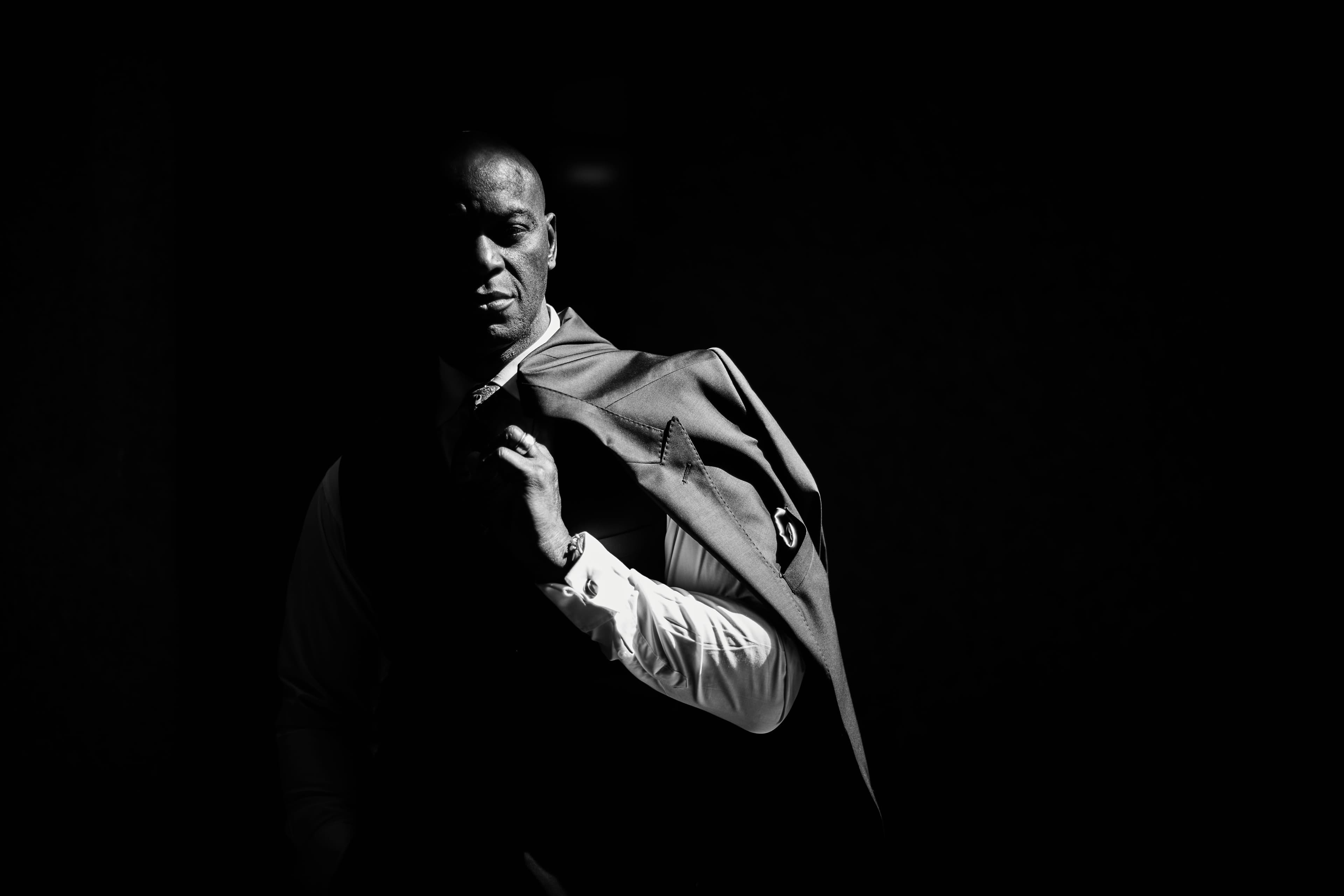 Ola Onabulé poses in a dark suit, half lit against a black background.