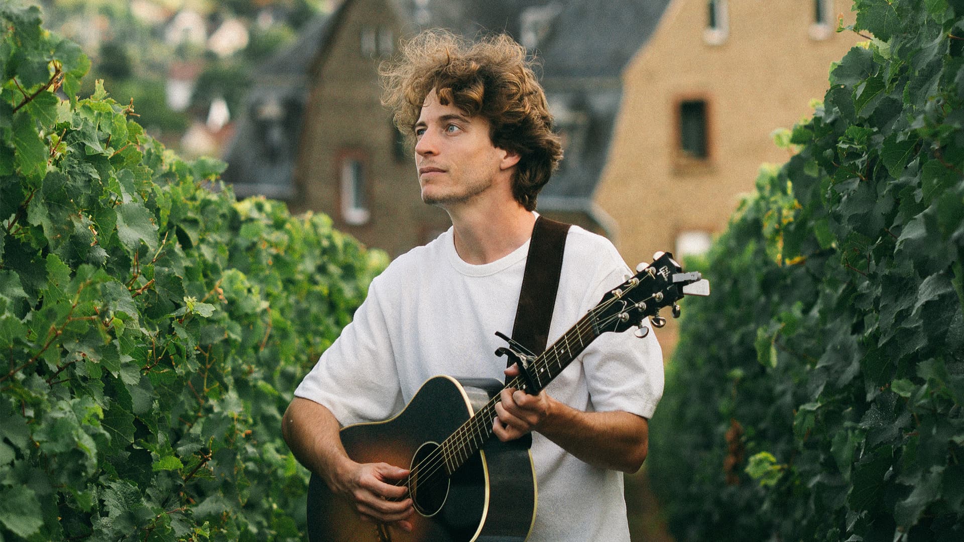 Portrait of the singer-songwriter Thaler holding an acoustic guitar.