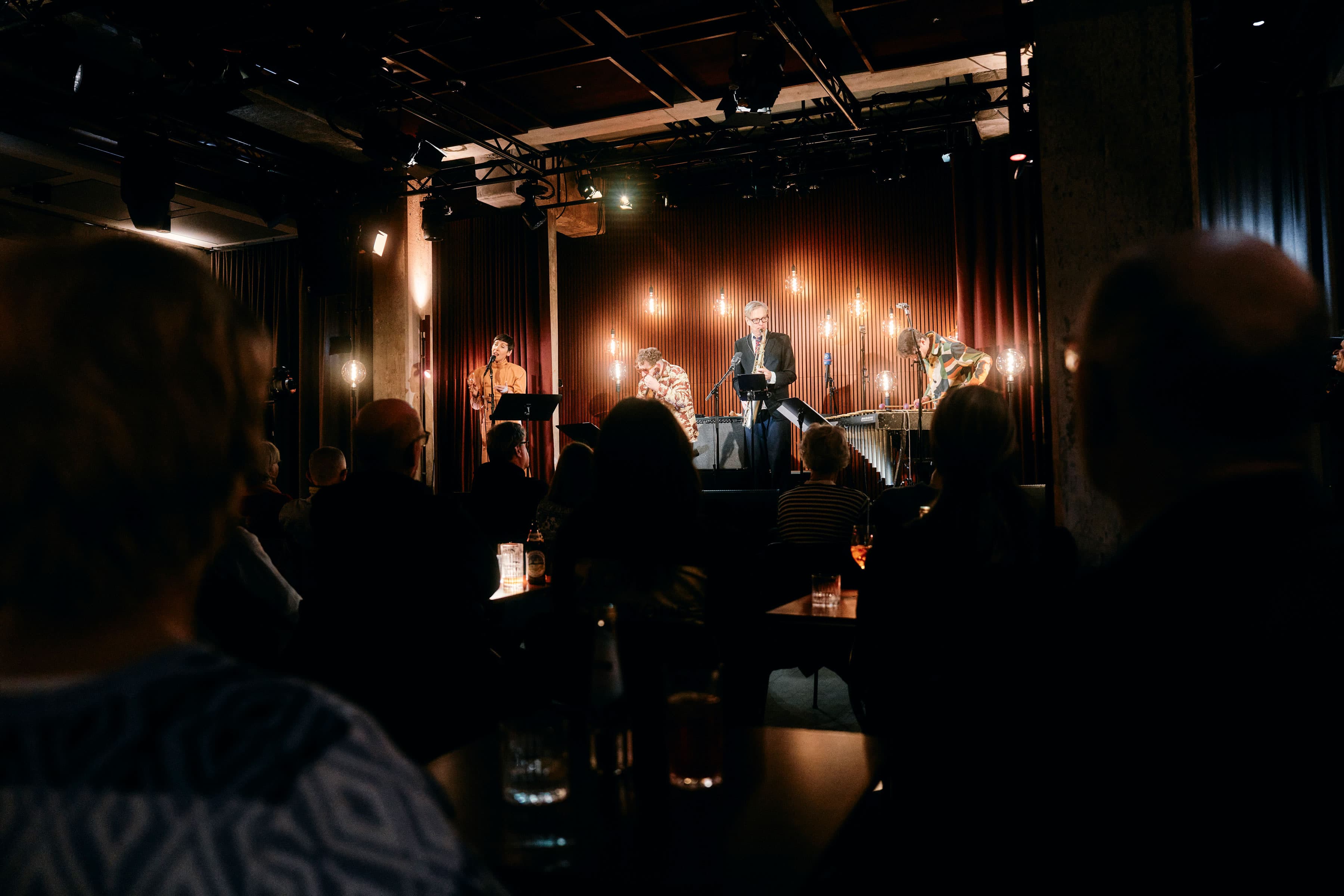 Musicians performing on a low stage in the dimly lit basement live club at Bergson.
