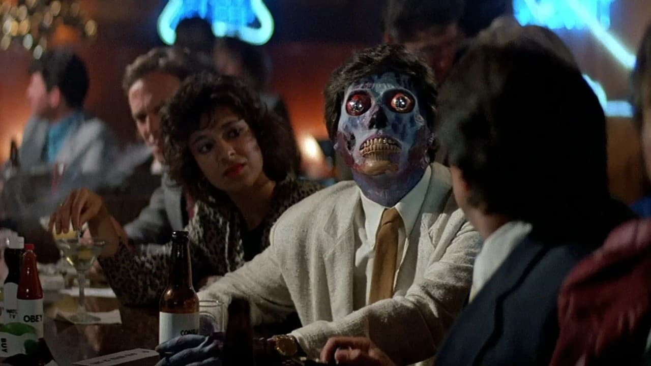 A person in a suit wearing a grotesque alien mask with bulging eyes sits at a bar in a dimly lit room.