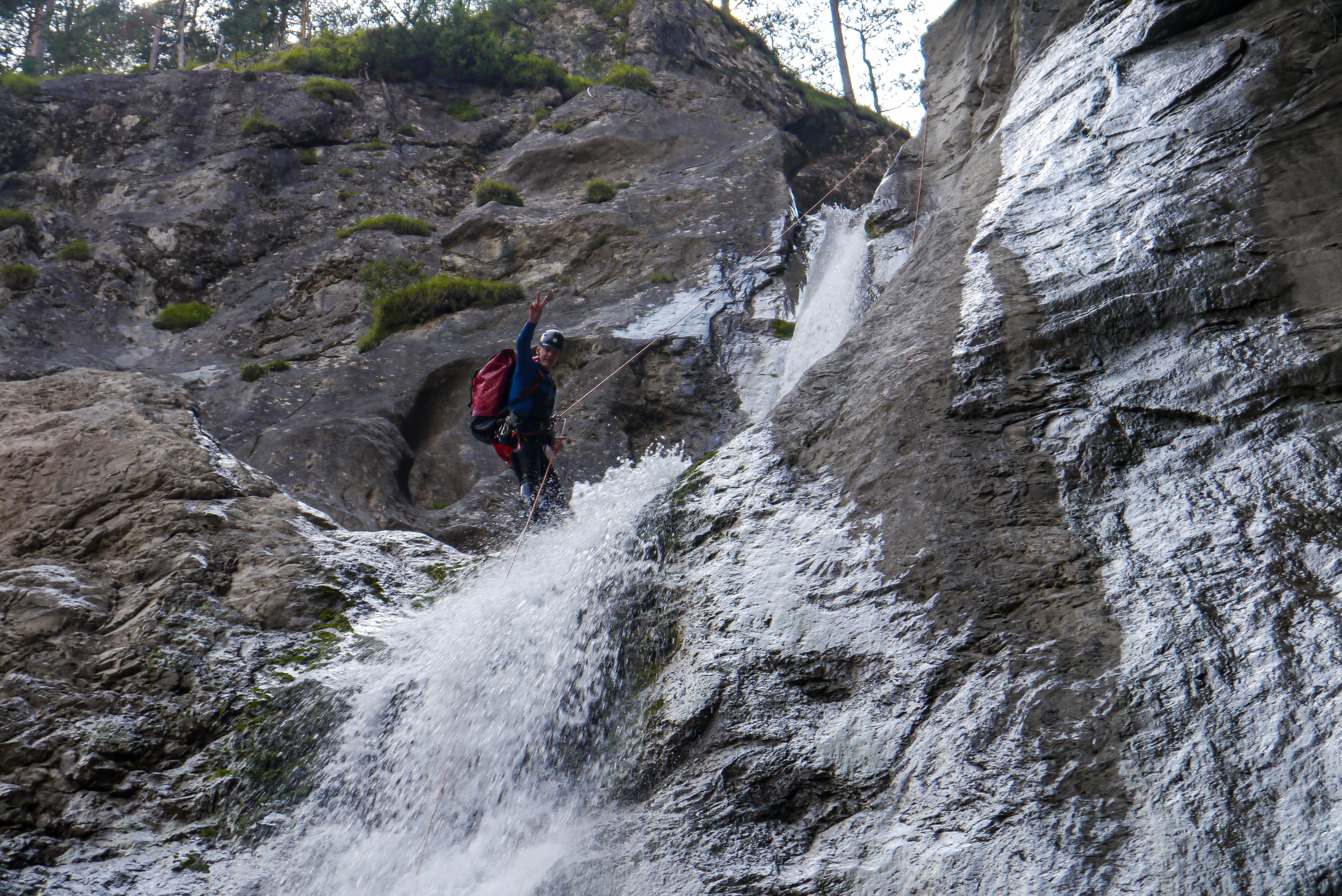 A canyoner abseiling beside a waterfall in a rocky gorge.