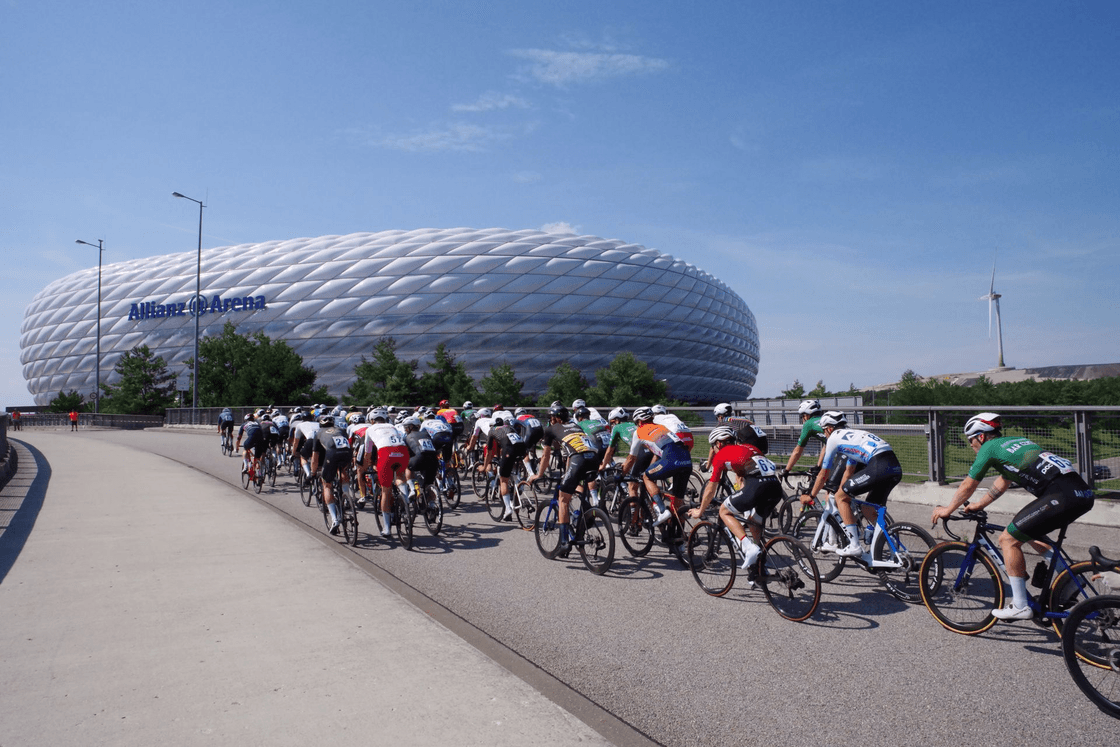 A road-racing peloton riding past the Allianz Arena.