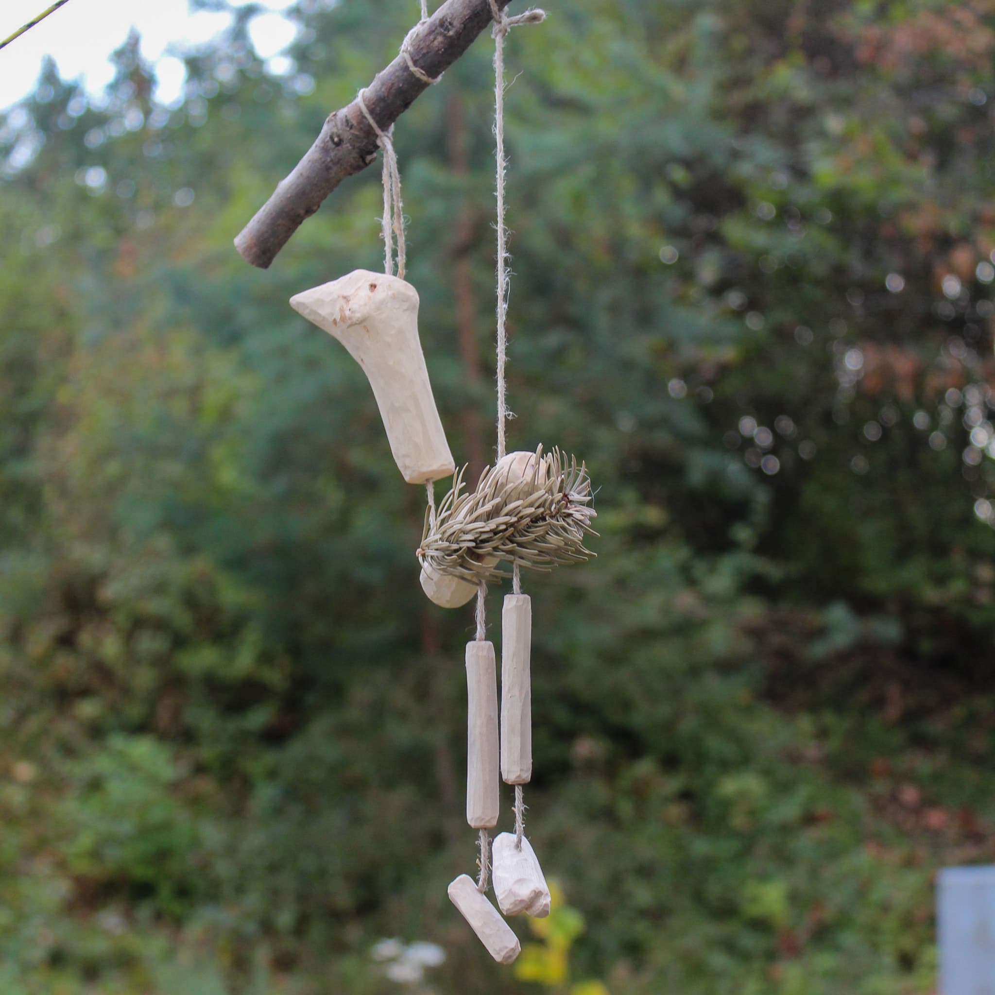 A handmade hanging bird sculpture carved from wood and woven natural fibres.