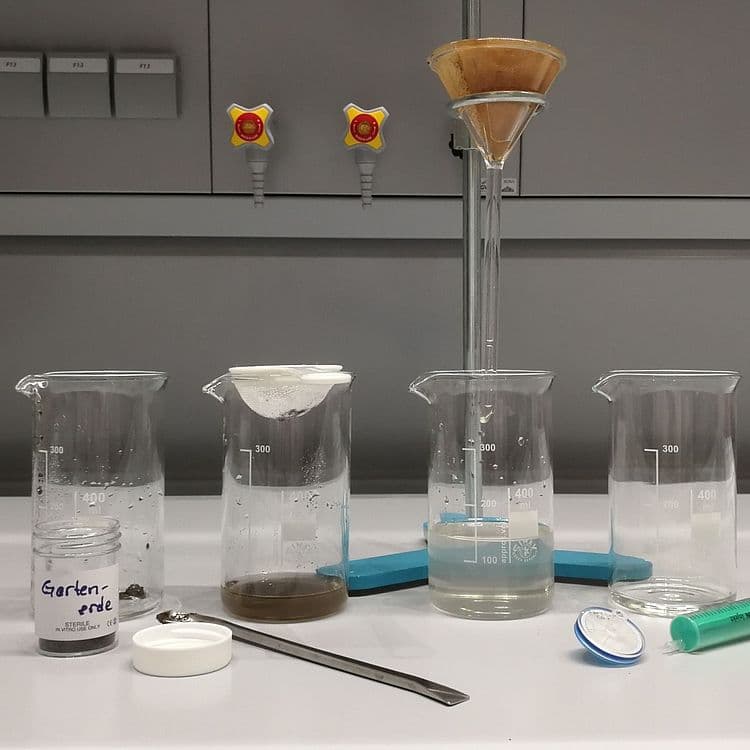 A home-made miniature water-treatment setup filters dirty water through several containers.