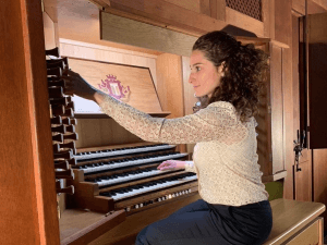 Sara Musumeci seated at an organ console, reaching towards the stops.
