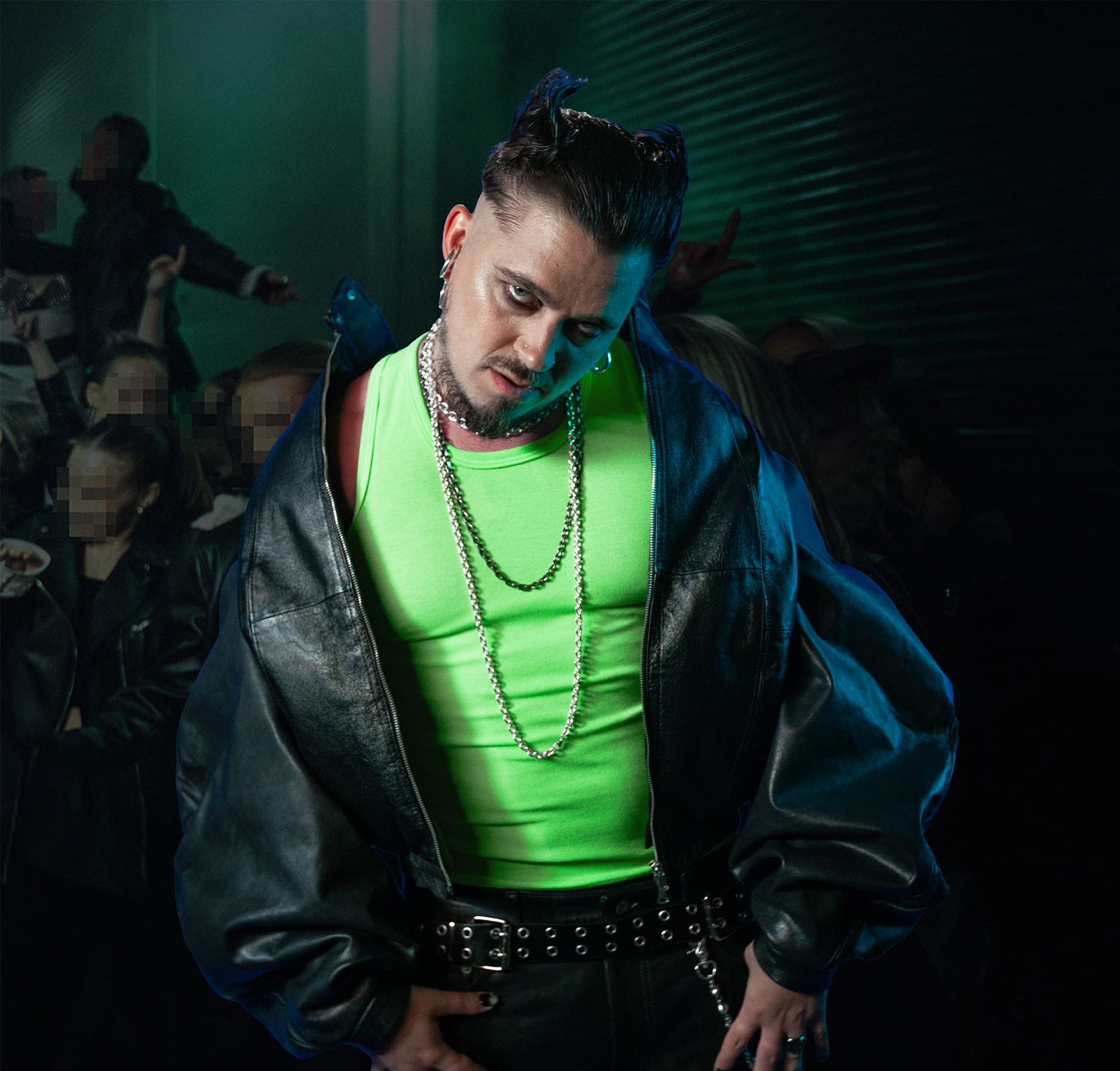 Käärijä in a neon-green vest and black leather jacket, lit blue and green, standing in front of a crowd.