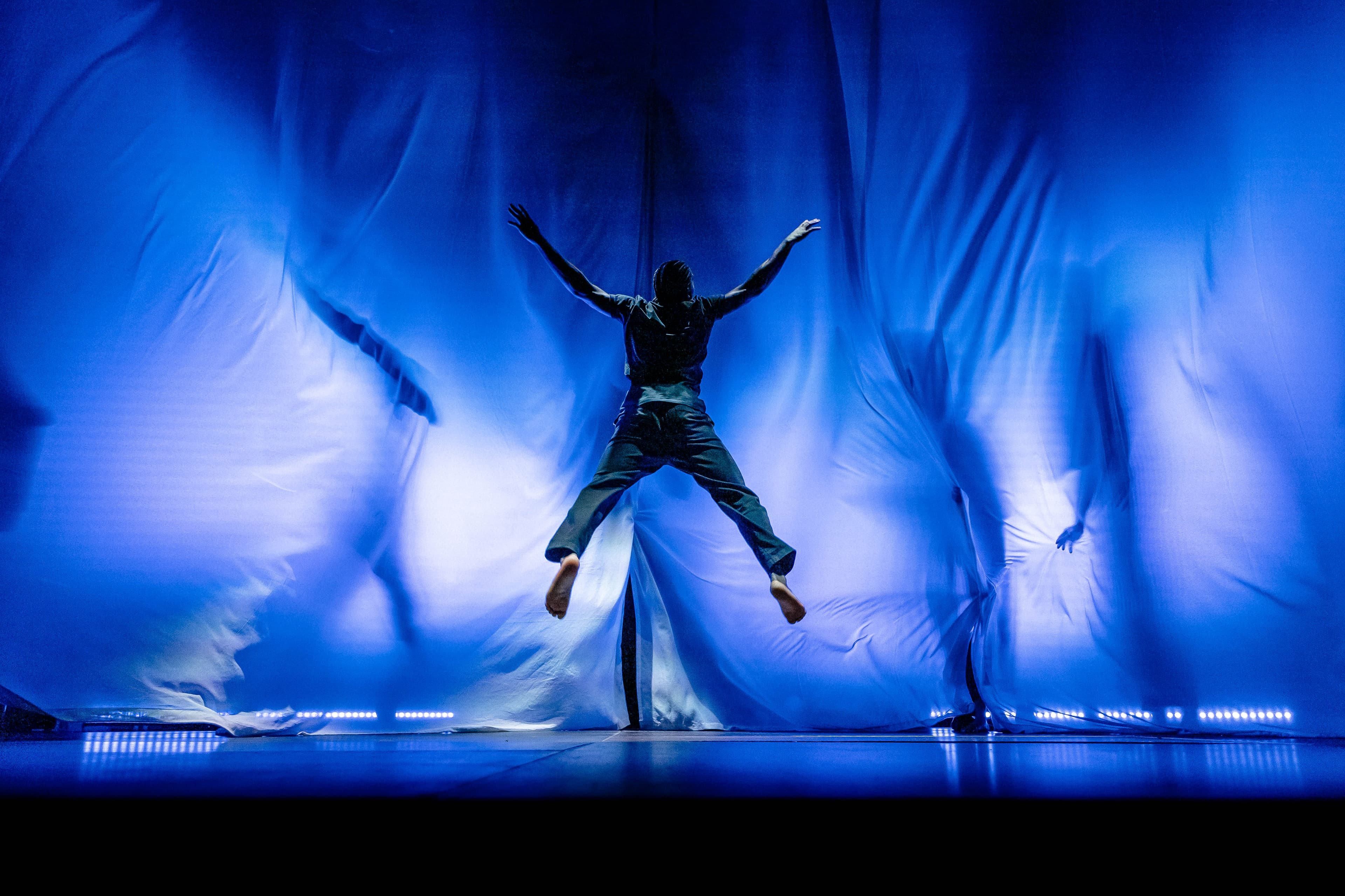 Performers of the Theater Grenzenlos production Mut on a dim stage, using movement and shadow to evoke people waiting by the sea.